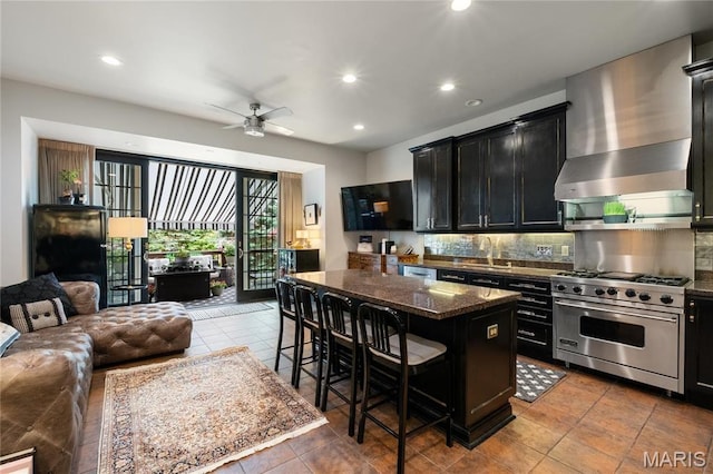 kitchen featuring luxury stove, dark cabinetry, open floor plan, a breakfast bar, and decorative backsplash