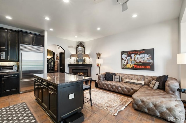 kitchen featuring stainless steel built in fridge, arched walkways, open floor plan, a breakfast bar area, and a lit fireplace