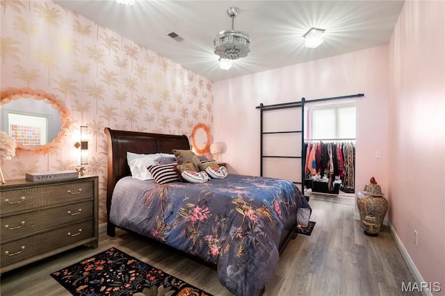 bedroom featuring wallpapered walls, baseboards, wood finished floors, and a barn door