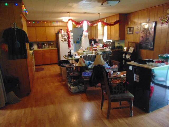 kitchen with freestanding refrigerator, light wood-style flooring, brown cabinets, wood walls, and pendant lighting