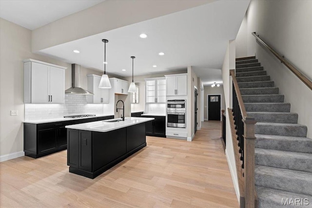 710 Angenette Ave, Kirkwood, MO 63122 - kitchen with wall chimney exhaust hood, dark cabinets, double oven, light wood finished floors, and light countertops