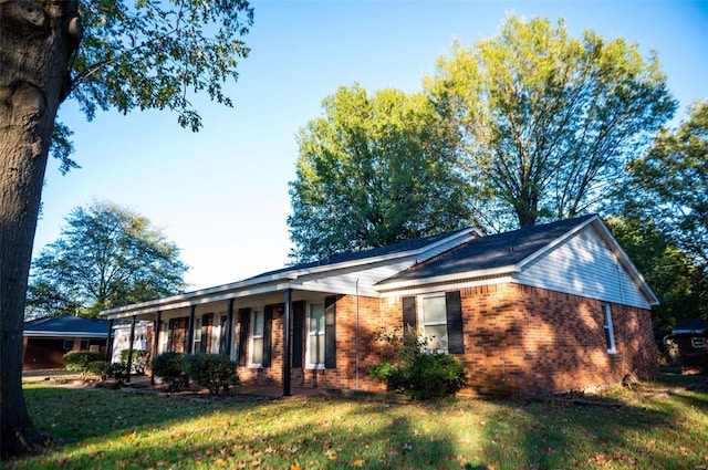 view of side of property featuring a yard, brick siding, and covered porch