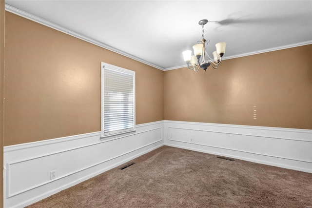 empty room featuring a chandelier, ornamental molding, wainscoting, and dark colored carpet