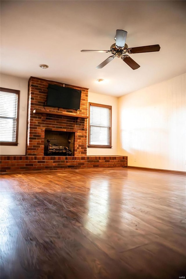 unfurnished living room with a brick fireplace, wood finished floors, healthy amount of natural light, and a ceiling fan