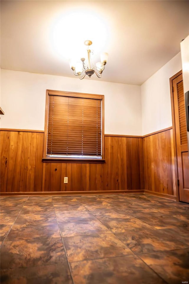 unfurnished room with wood walls, a chandelier, and a wainscoted wall