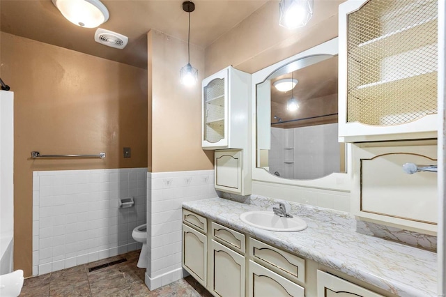 bathroom with vanity, tile walls, toilet, a shower, and a wainscoted wall