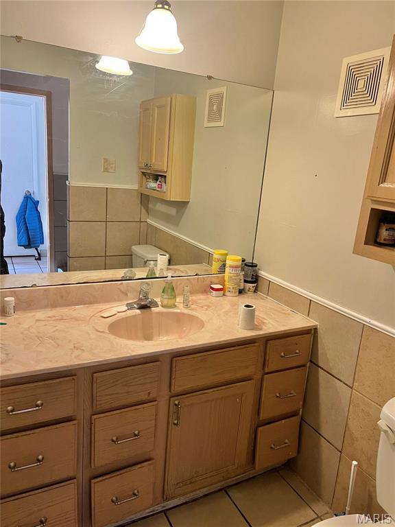 7262 Hazelcrest Dr, Hazelwood, MO 63042 - half bathroom featuring tile walls, toilet, vanity, a wainscoted wall, and tile patterned floors