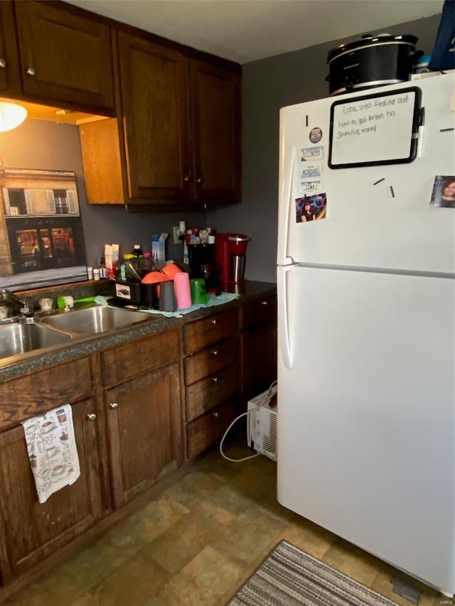 kitchen with freestanding refrigerator, a sink, and dark countertops