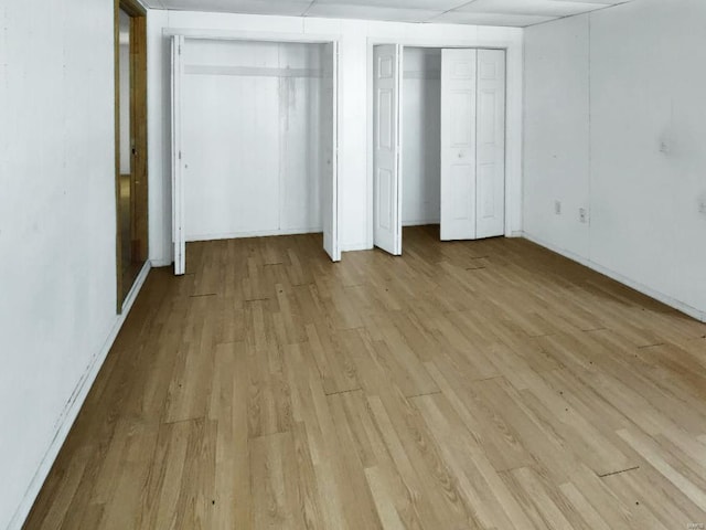 unfurnished bedroom with light wood-style floors, multiple closets, and baseboards
