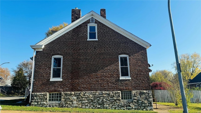 view of side of property with a chimney, brick siding, and fence