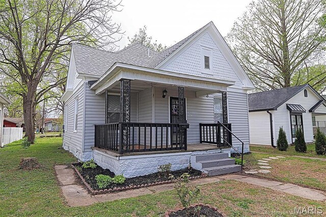 victorian house featuring covered porch, roof with shingles, and a front lawn