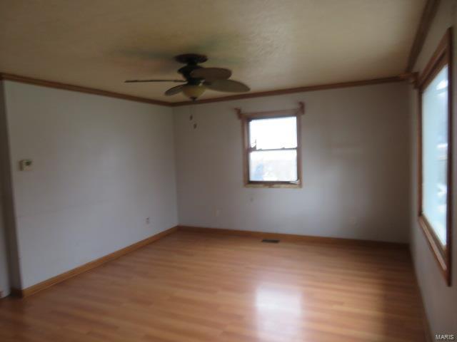 spare room with light wood-style floors, a ceiling fan, crown molding, and baseboards