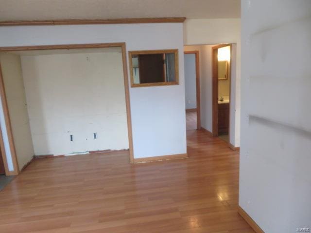 empty room featuring light wood-type flooring, crown molding, and baseboards