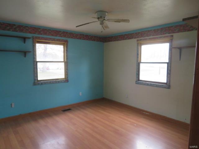 unfurnished room with light wood-style flooring, a ceiling fan, healthy amount of natural light, and baseboards