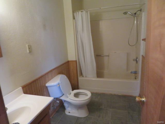 full bathroom with wainscoting, toilet, vanity, shower / tub combo, and wooden walls