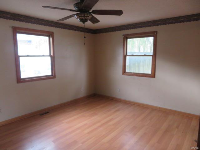 empty room featuring plenty of natural light, light wood finished floors, ceiling fan, and baseboards
