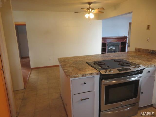 817 S Montgomery Ave, Litchfield, IL 62056 - kitchen with stainless steel range with electric cooktop, a ceiling fan, a peninsula, white cabinets, and light stone countertops