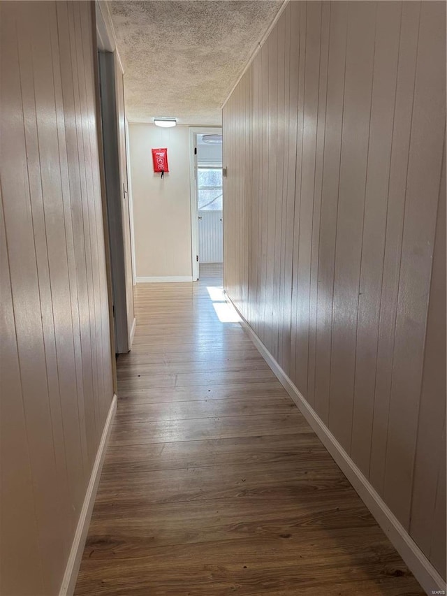 corridor featuring baseboards, wood finished floors, a textured ceiling, and wood walls