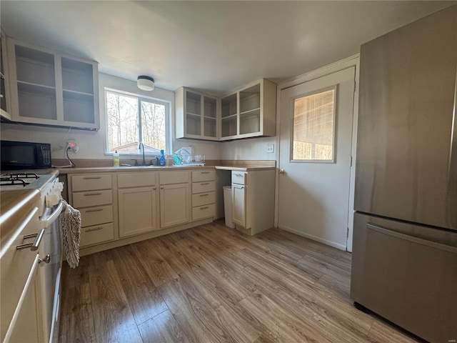 kitchen with freestanding refrigerator, black microwave, white range with gas cooktop, light wood-style flooring, and a sink
