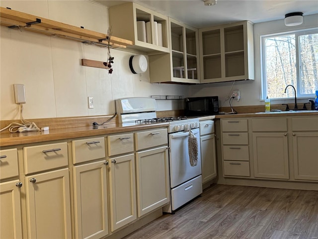kitchen with white gas range oven, open shelves, black microwave, a sink, and wood finished floors