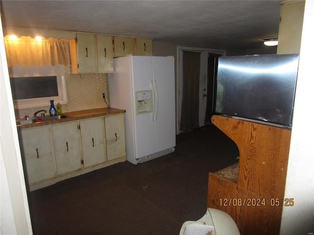 kitchen featuring white refrigerator with ice dispenser, a sink, and cream cabinetry