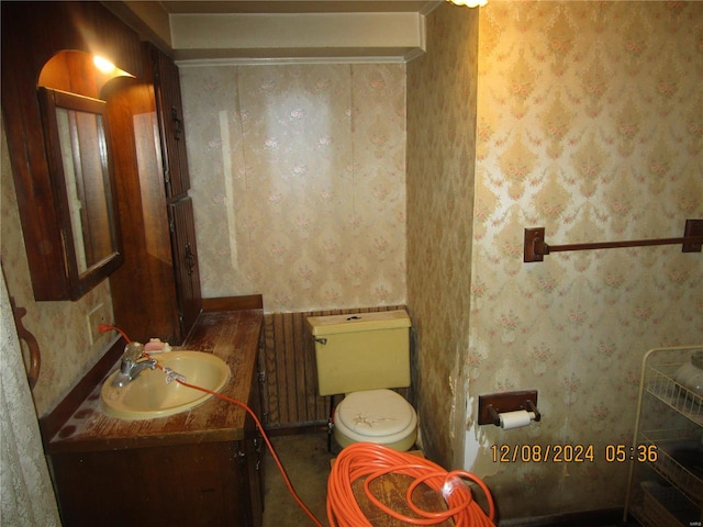 half bathroom featuring toilet, vanity, and wallpapered walls