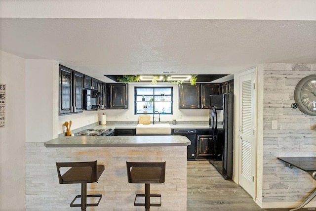 kitchen featuring a sink, black appliances, a peninsula, a kitchen breakfast bar, and light wood-type flooring