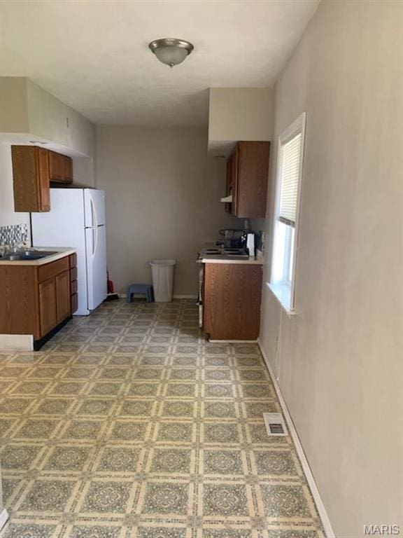 kitchen with brown cabinets, freestanding refrigerator, light flooring, light countertops, and stainless steel range with electric cooktop