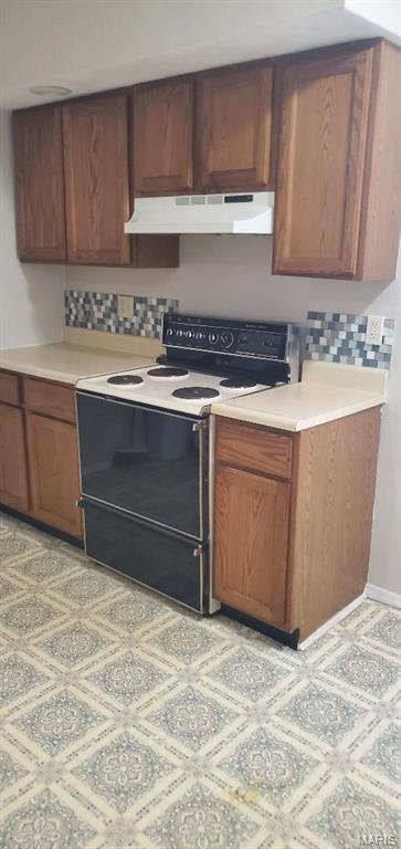 kitchen with electric range, under cabinet range hood, decorative backsplash, and light countertops