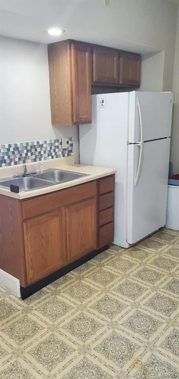 kitchen with freestanding refrigerator, a sink, light countertops, tasteful backsplash, and brown cabinetry