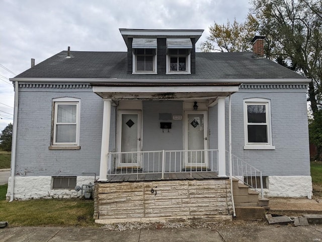 view of front of home with brick siding, covered porch, and a chimney