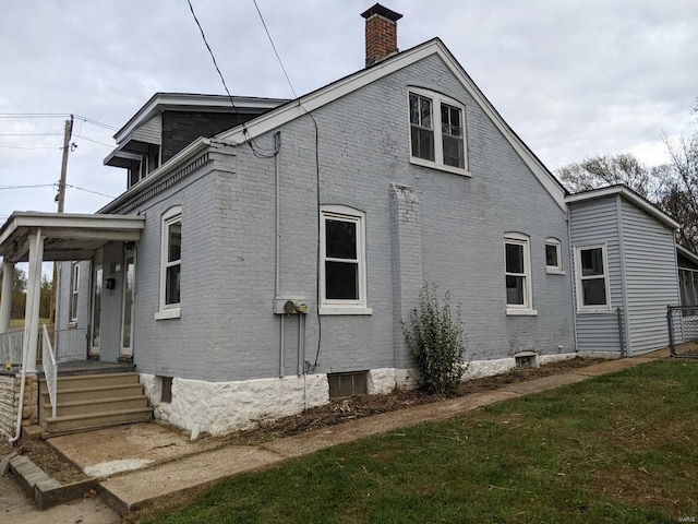 view of home's exterior with brick siding, a chimney, and a lawn