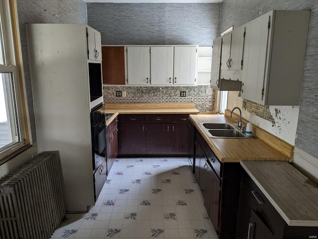 kitchen featuring radiator heating unit, a sink, decorative backsplash, light countertops, and white cabinetry