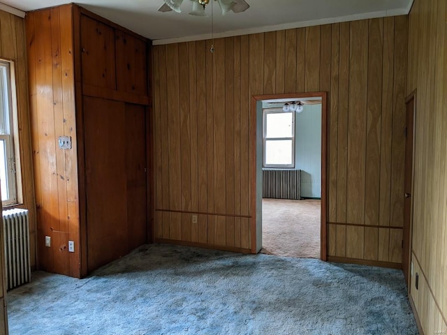 empty room featuring carpet floors, radiator heating unit, ceiling fan, and wood walls