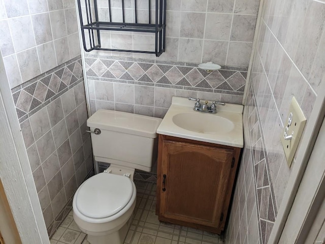 half bathroom with tile walls, vanity, toilet, and tile patterned flooring
