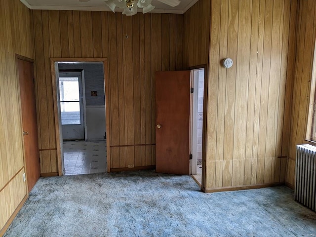carpeted spare room with radiator, wooden walls, ceiling fan, and ornamental molding
