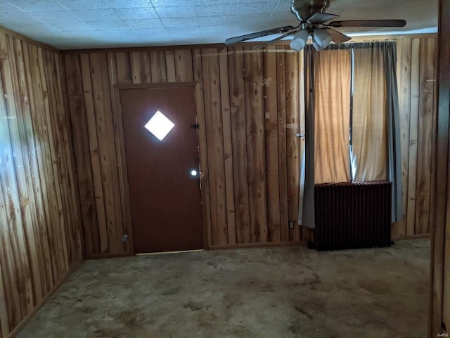 foyer entrance featuring radiator heating unit, a ceiling fan, carpet floors, and wood walls