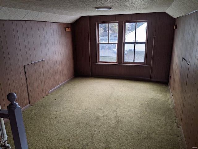 additional living space featuring vaulted ceiling, wooden walls, and light colored carpet