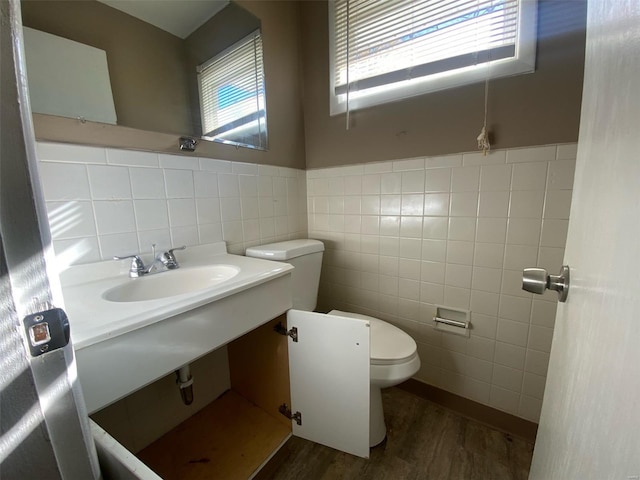 bathroom featuring tile walls, wood finished floors, toilet, and a sink