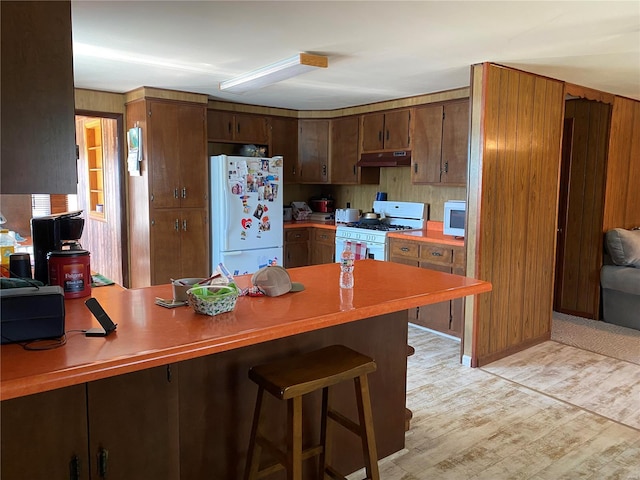 kitchen featuring white appliances, under cabinet range hood, a peninsula, light wood finished floors, and light countertops