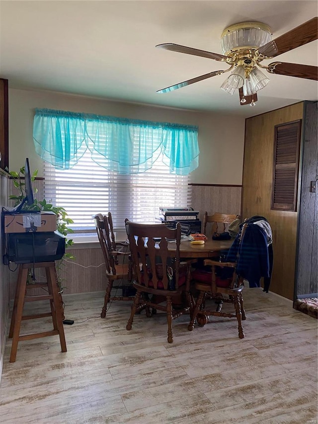 dining space featuring light wood-style floors, ceiling fan, and wooden walls