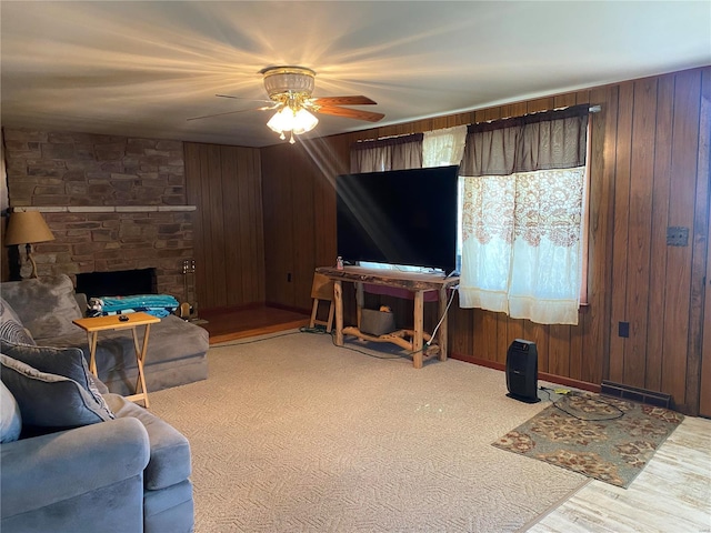 living area with a ceiling fan, wood walls, and a stone fireplace