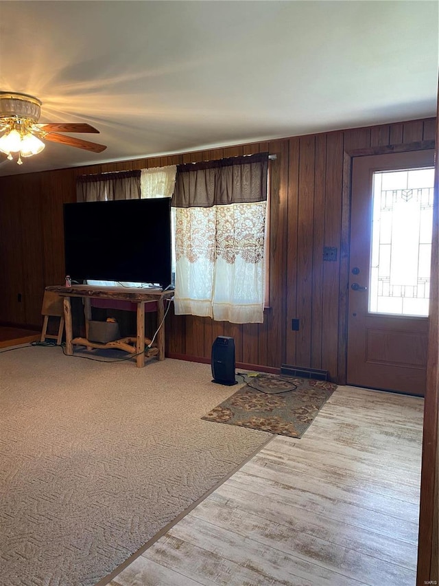 living room with wooden walls, a ceiling fan, and wood finished floors