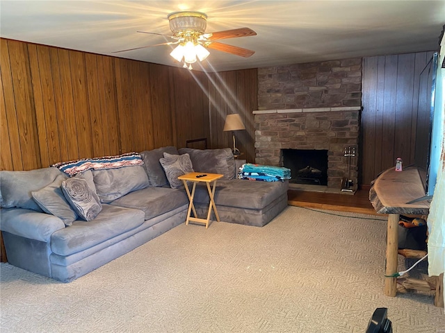 living room with wood walls, ceiling fan, carpet, and a stone fireplace