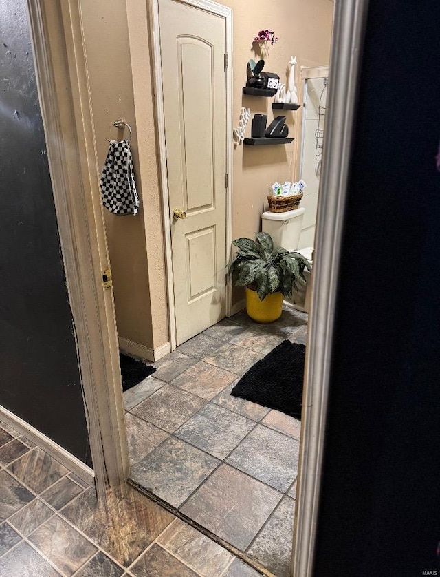 hall featuring stone tile flooring and baseboards