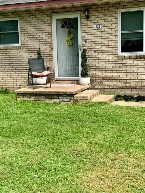 doorway to property featuring brick siding and a lawn