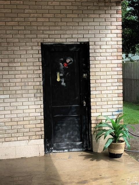 view of exterior entry featuring fence and brick siding