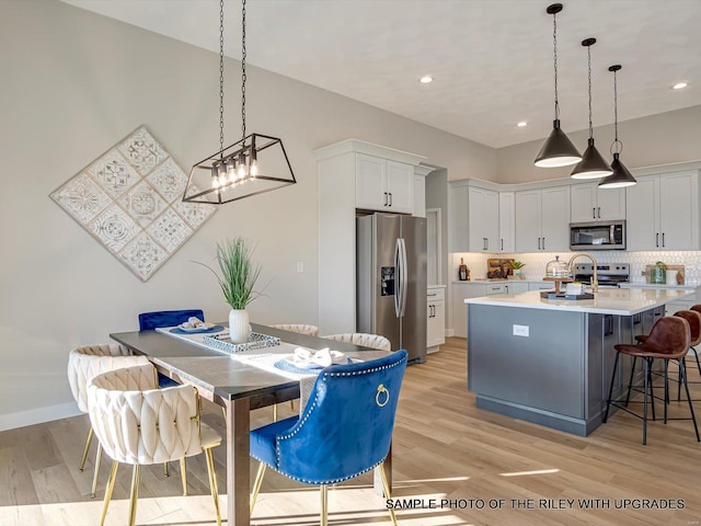 428 Hayden Dr, Waterloo, IL 62298 - kitchen featuring appliances with stainless steel finishes, light wood-style flooring, light countertops, backsplash, and a kitchen island with sink