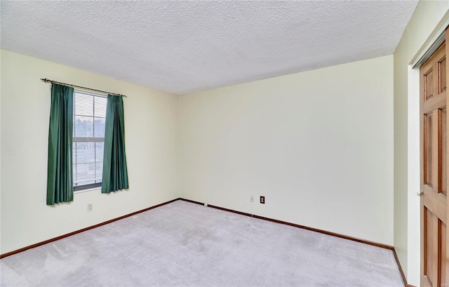 empty room with light carpet, baseboards, and a textured ceiling