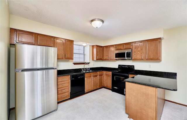 kitchen with black appliances, a peninsula, a sink, brown cabinets, and dark stone counters